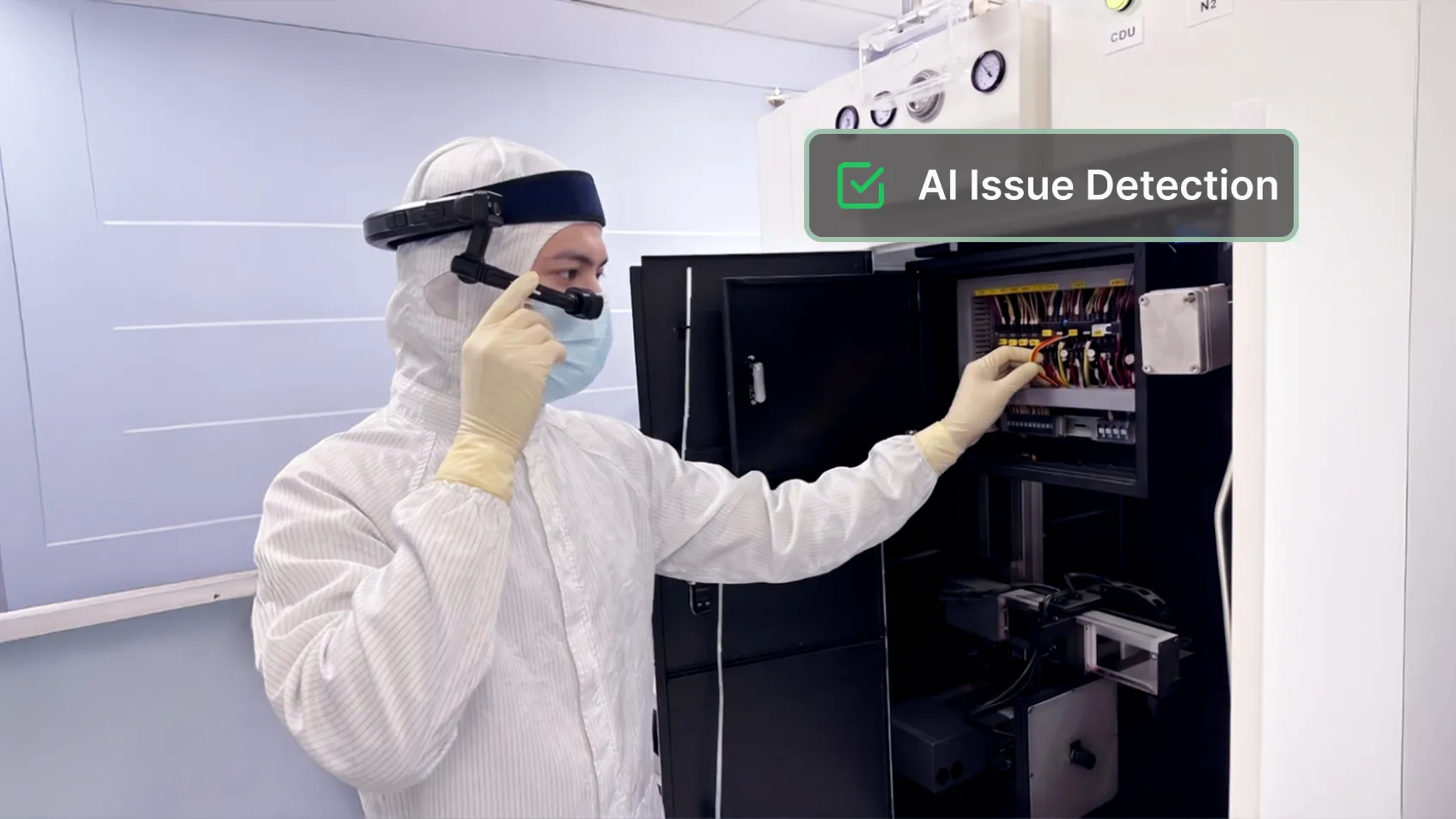 A technician in a cleanroom suit wearing smart glasses inspects an equipment cabinet.